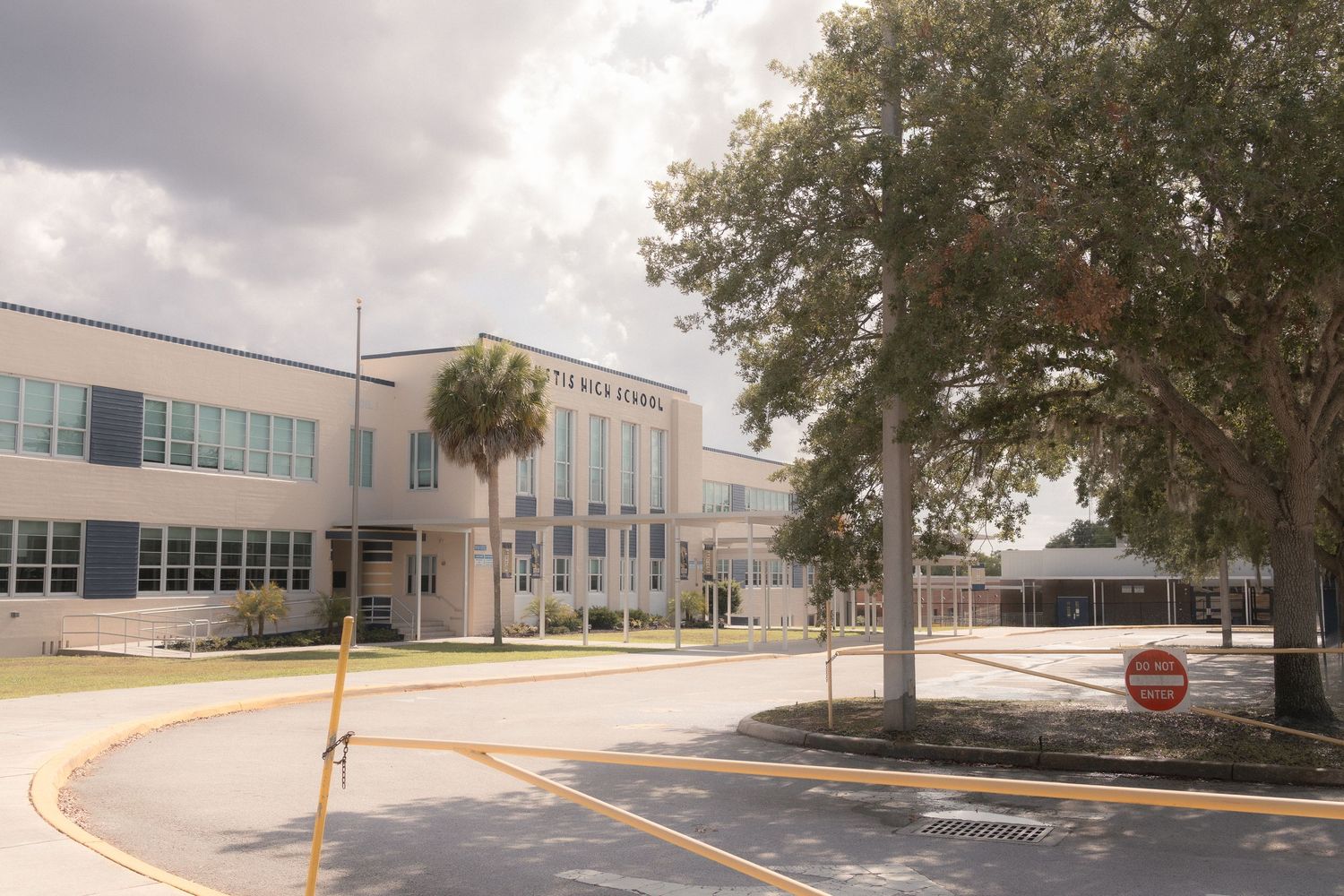 Modern school building with palm trees, stop sign, and cloudy sky in a Florida suburban campus setting.