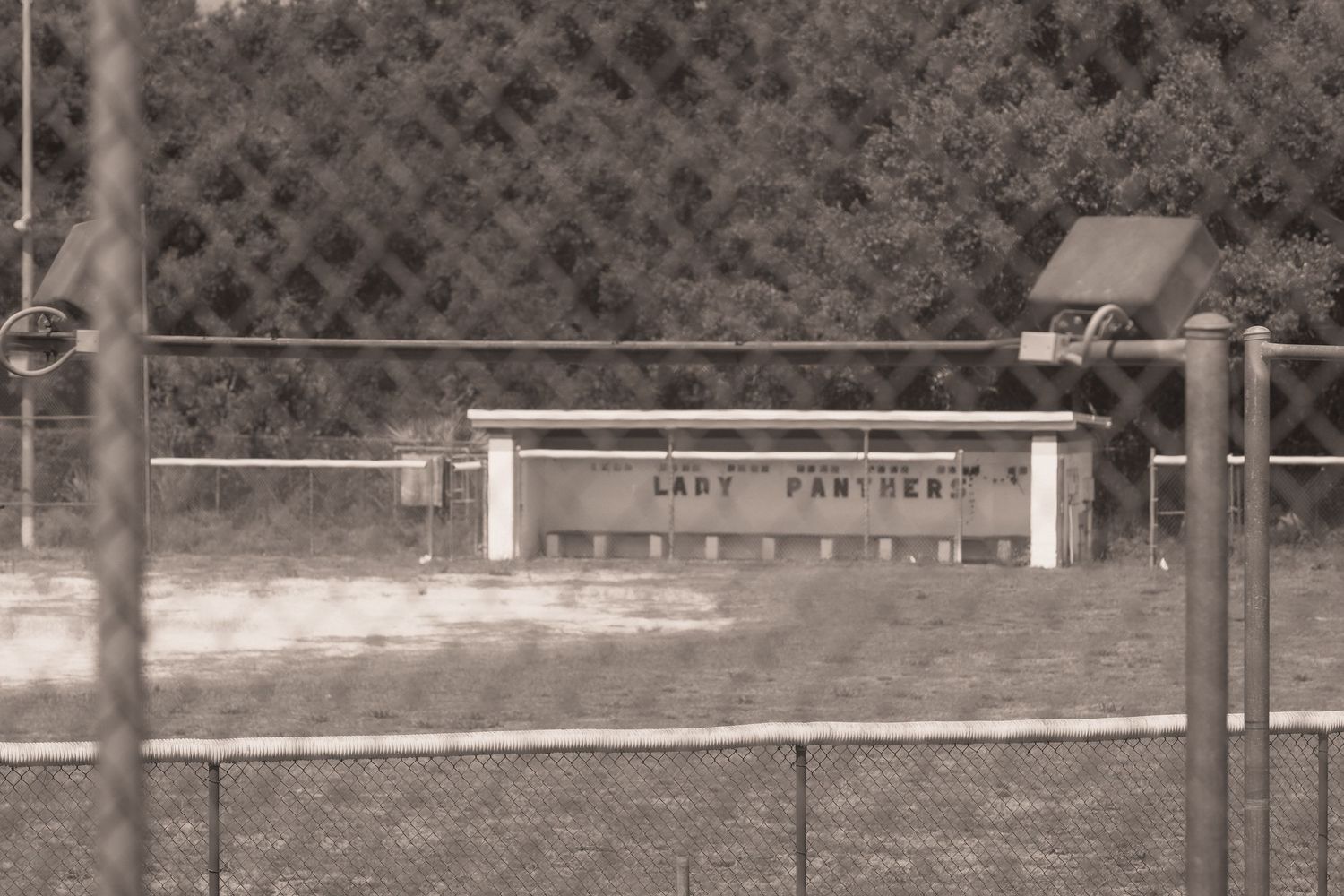 Sepia-toned photo of a Lady Panthers dugout bench behind a chain-link fence at an outdoor sports field.