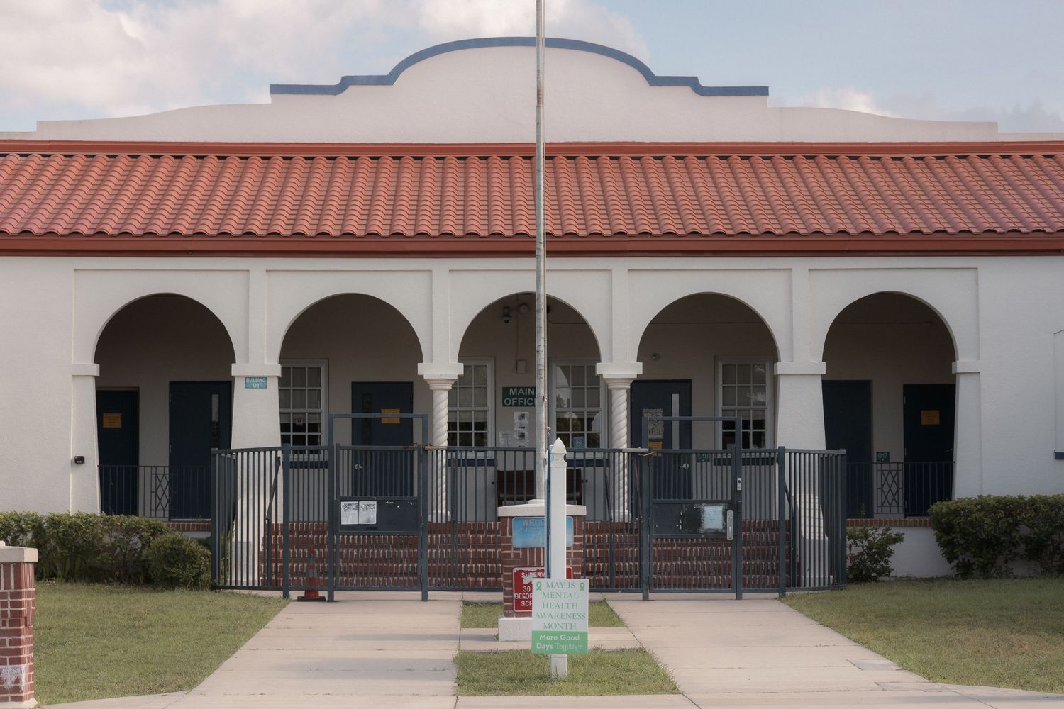 White stucco building with red tile roof, arched entryways, and decorative railings in a Spanish Colonial Revival style.