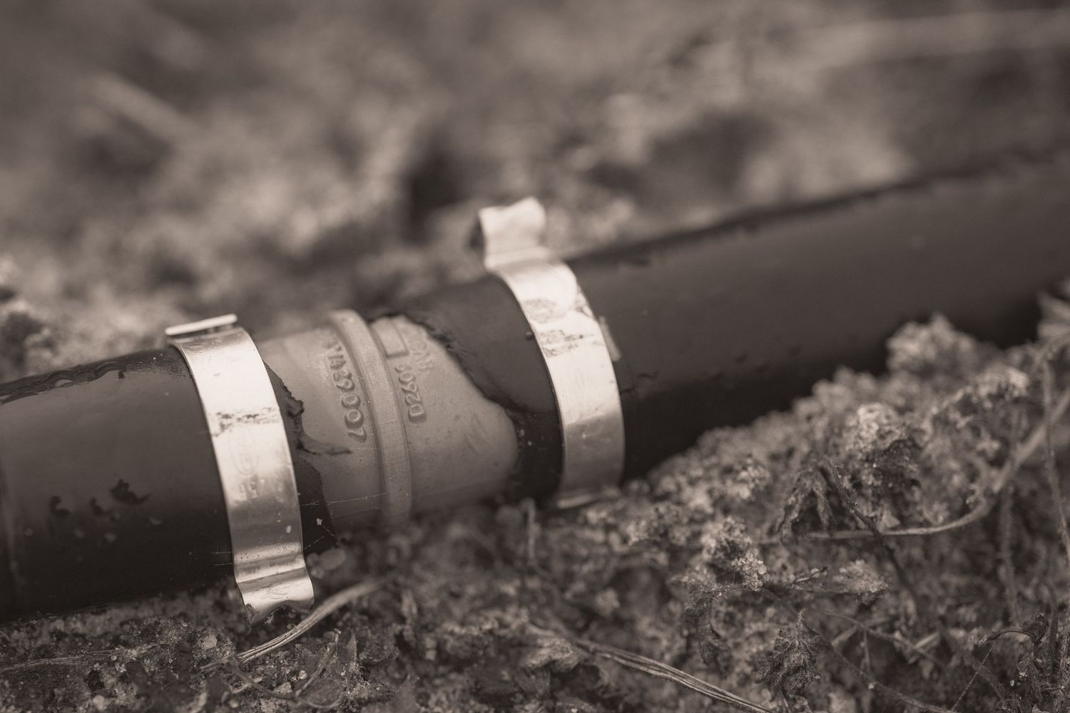 Close-up black and white photograph of a camera lens with metal rings lying on a textured surface.