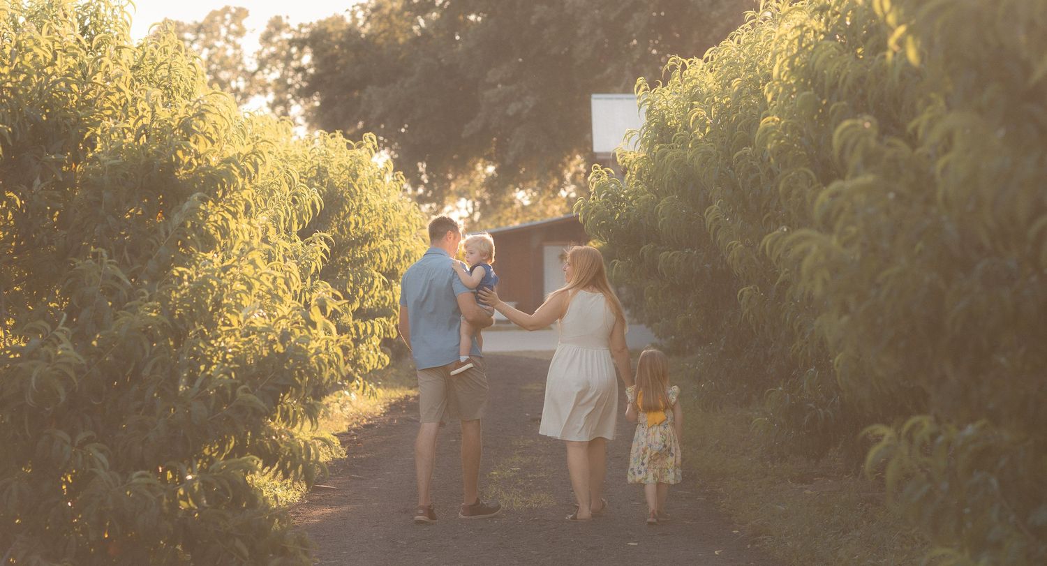 Family walking down a sun-dappled garden path surrounded by lush green trees during golden hour.