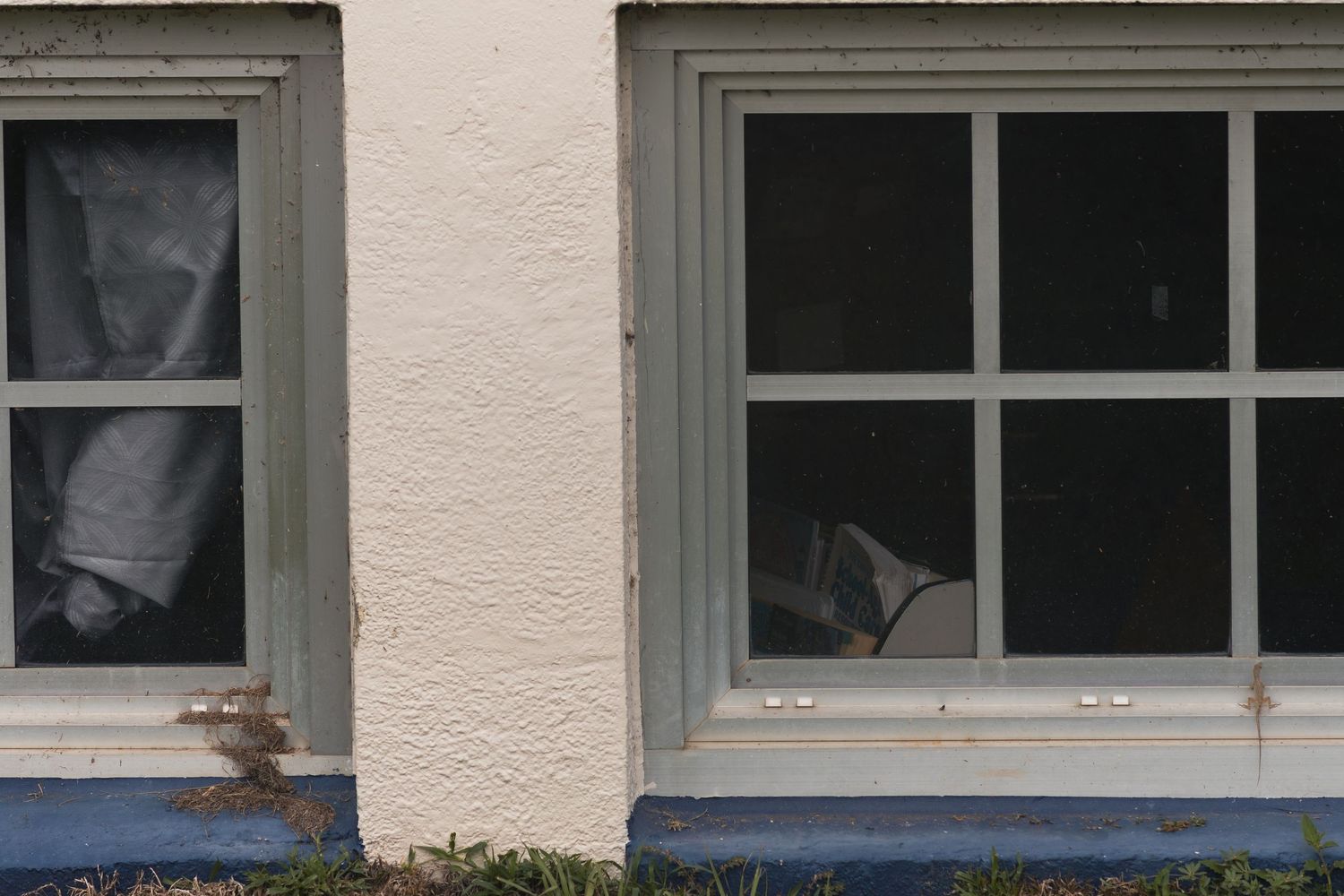 Two gray-framed windows on a white stucco building exterior with blue painted foundation trim.