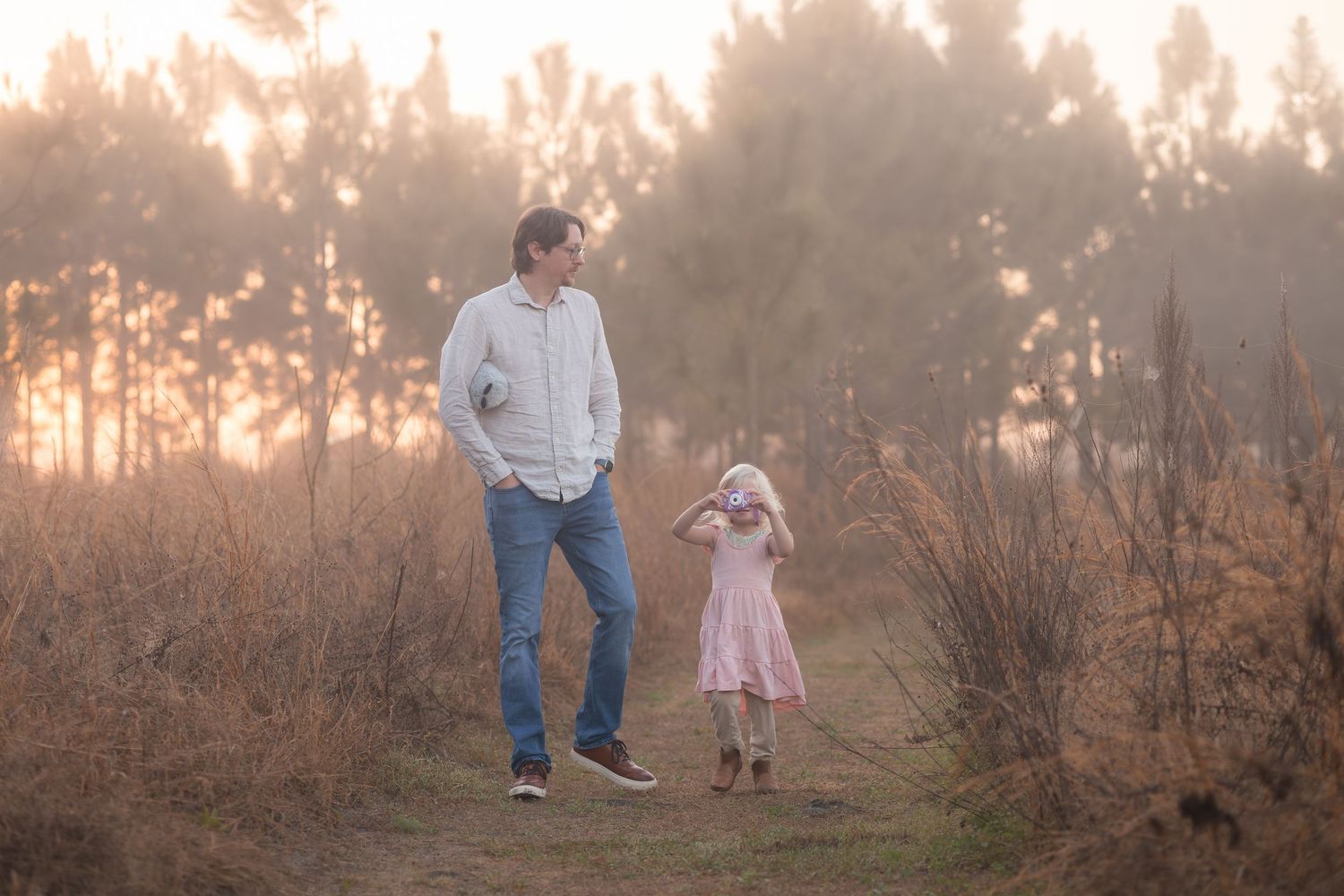 A parent and child walk together through a misty field at sunset while holding hands.