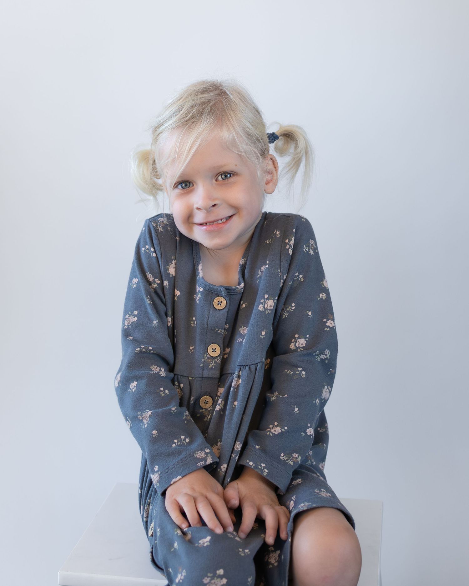 Child wearing a blue floral print outfit sits and plays on a white studio backdrop.
