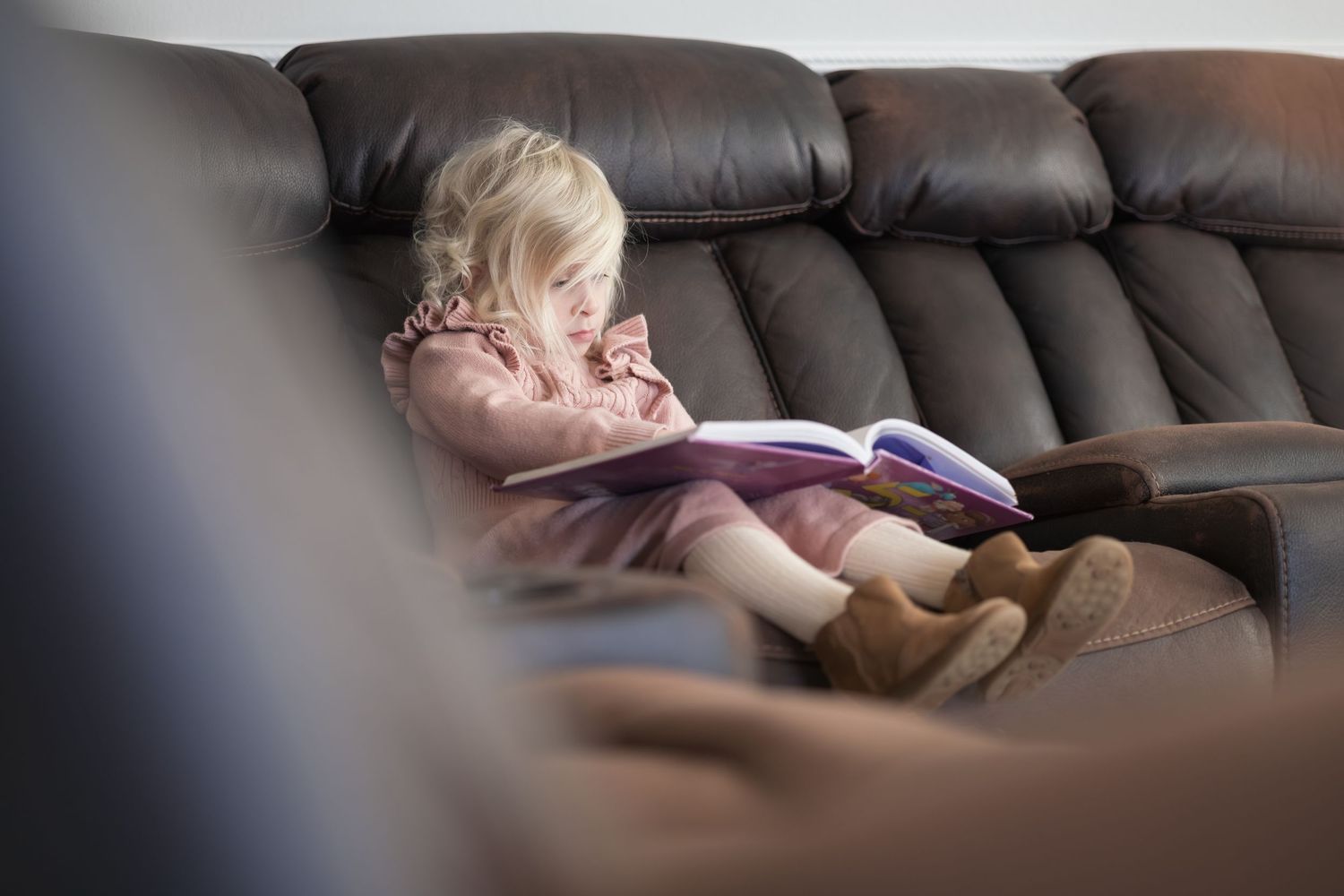 A person sleeping comfortably on a dark leather couch in a dimly lit room.