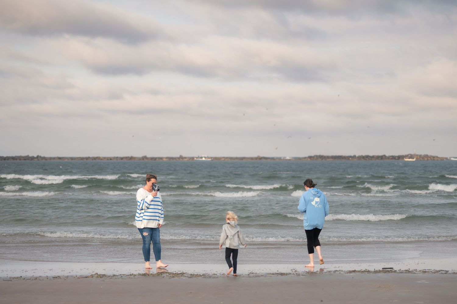 A scenic panoramic view of a beach with waves crashing on the shore and people walking along the water's edge.