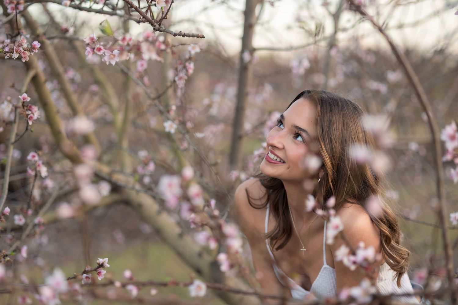 A person poses joyfully among blooming cherry blossom trees on a spring day.