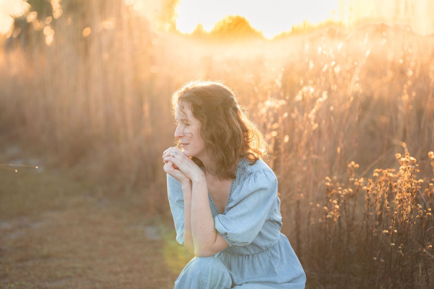 A woman in a flowy dress twirls through a sunlit field during golden hour creating a dreamy ethereal scene.
