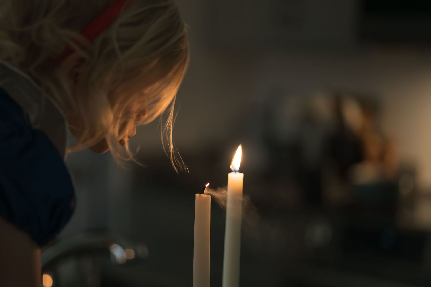 Burning candle with a soft glowing flame against a dark background creates a moody atmospheric scene.