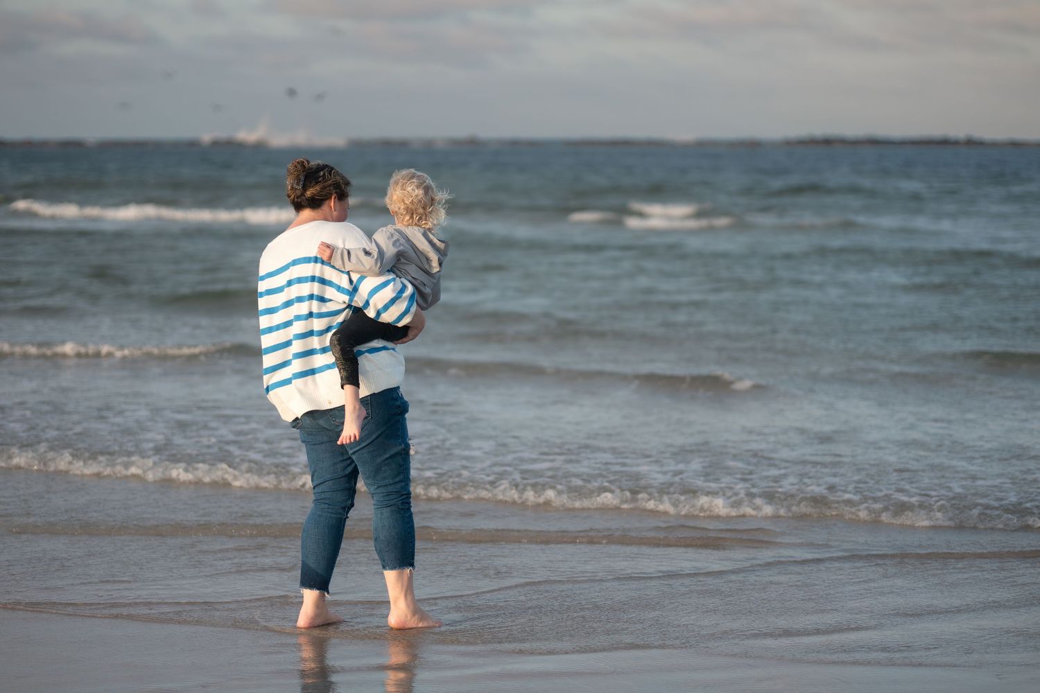 A couple embraces while walking along a sandy beach with ocean waves in the background.