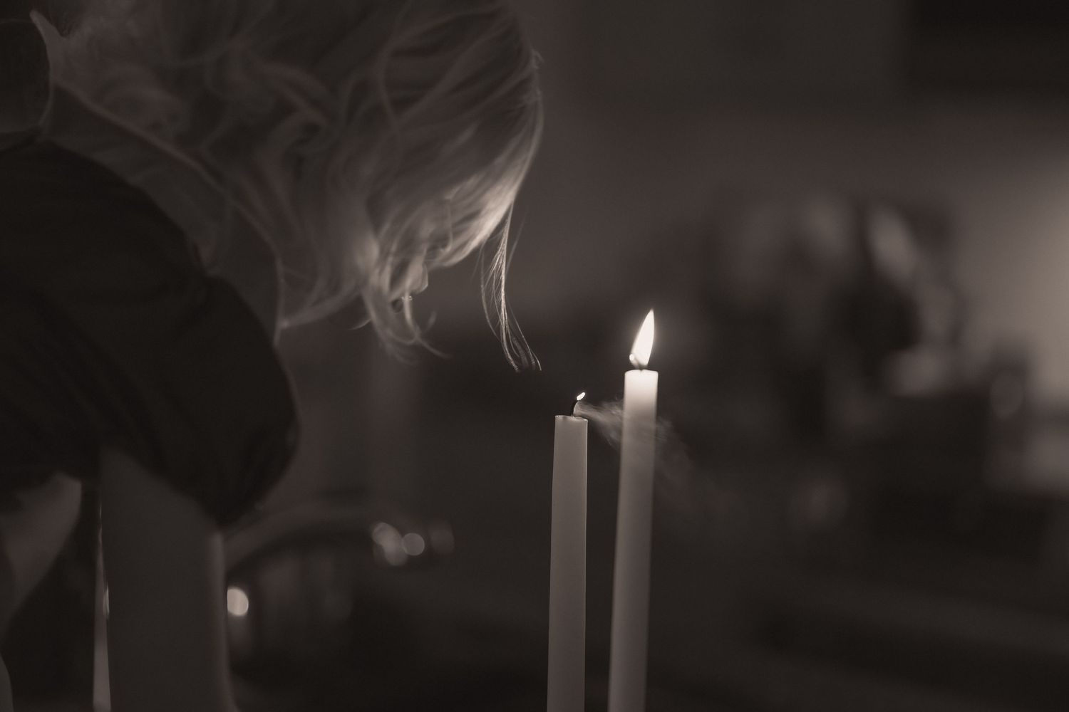 A series of dark, moody photographs showing lit candles with smoke trails rising against a black background.
