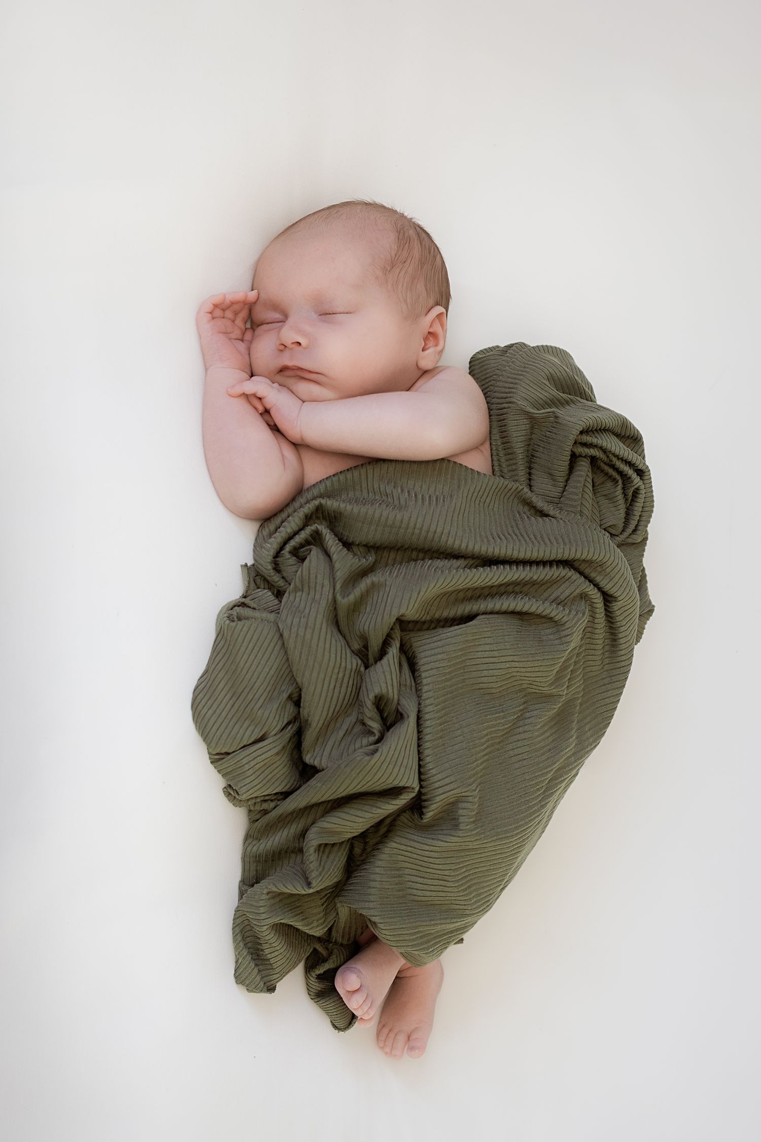 Sleeping baby wrapped in olive green swaddle blanket on white background shown from three different angles.