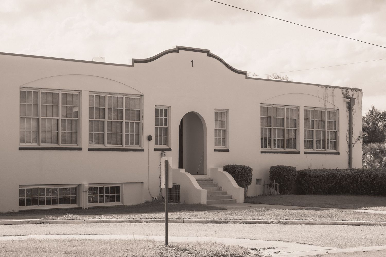 Vintage sepia photo of a classic white Art Deco school building with arched entrance and large windows.