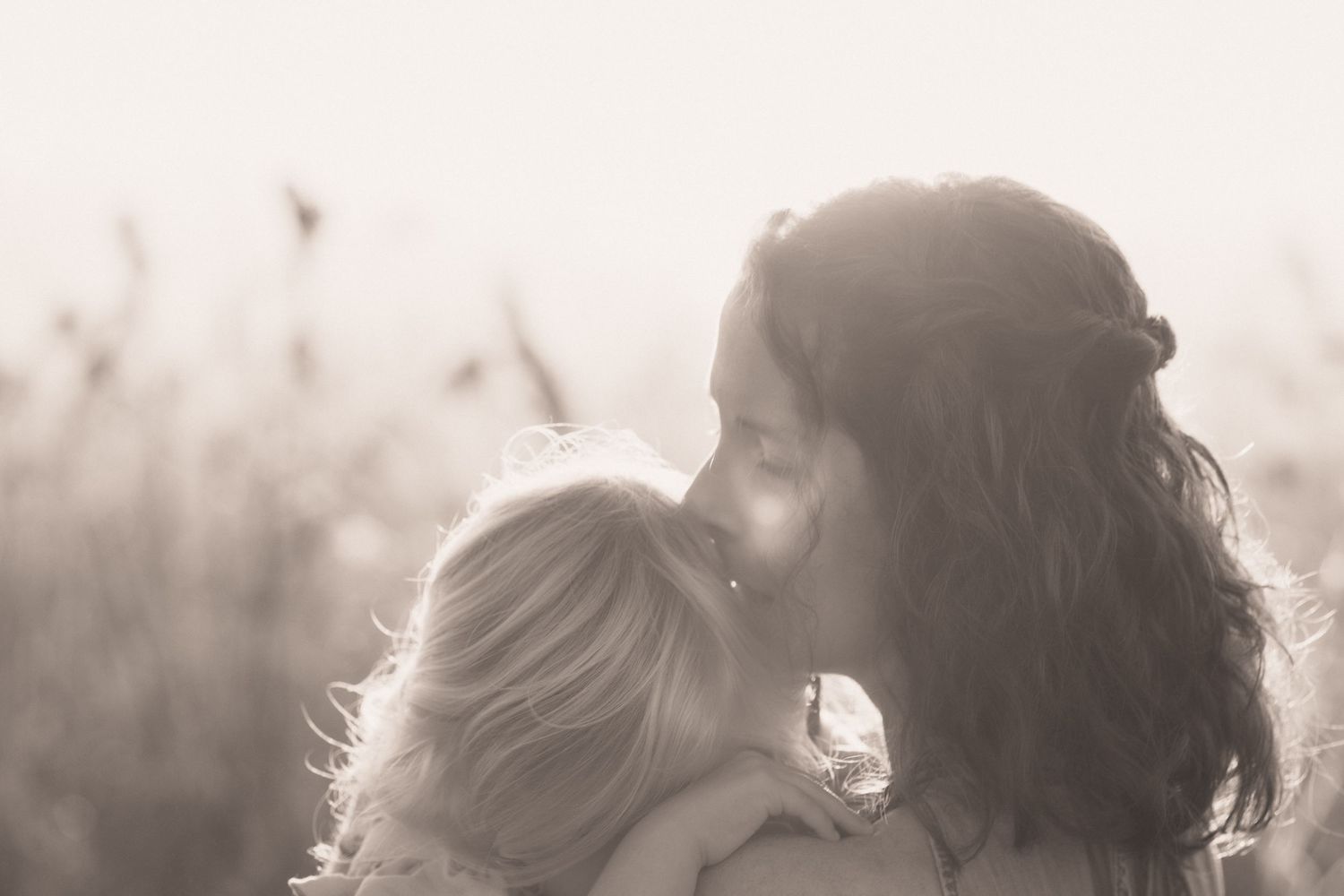 A silhouetted parent and child share a tender moment in soft sunlit backlighting.