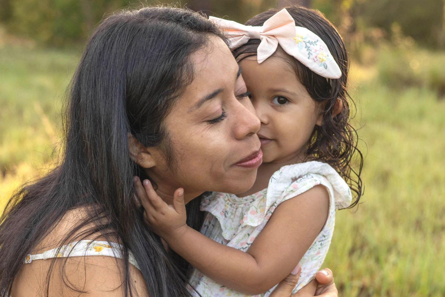 A tender moment shared between parent and child wearing white as they embrace in a sunlit meadow.