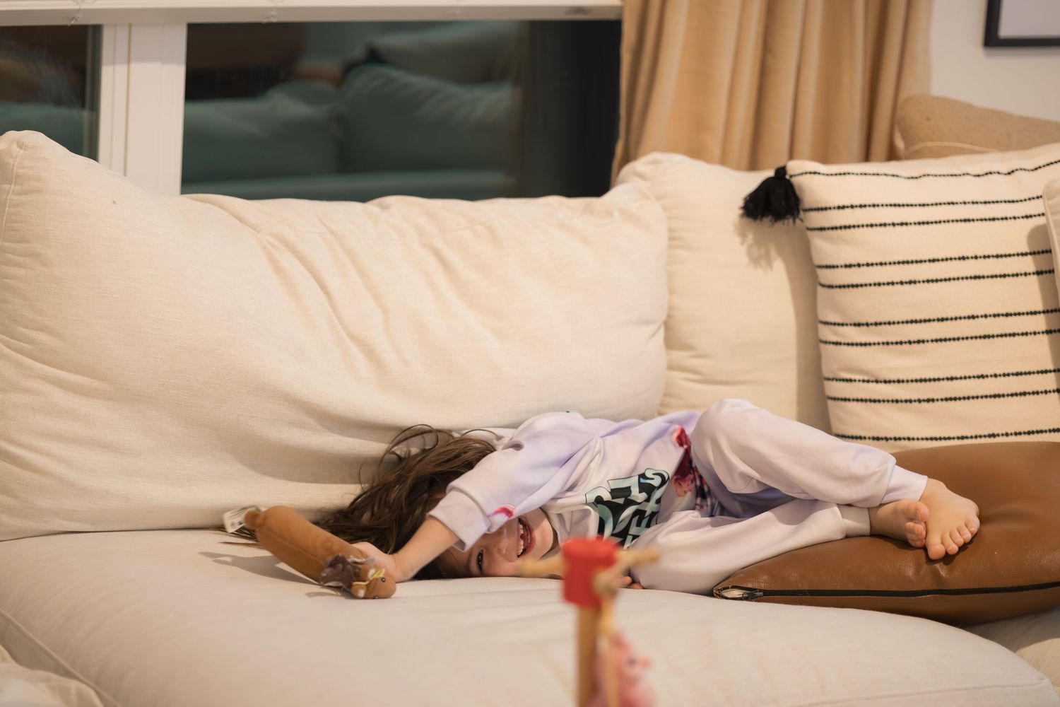 A child lies sprawled out on a beige couch with decorative pillows.