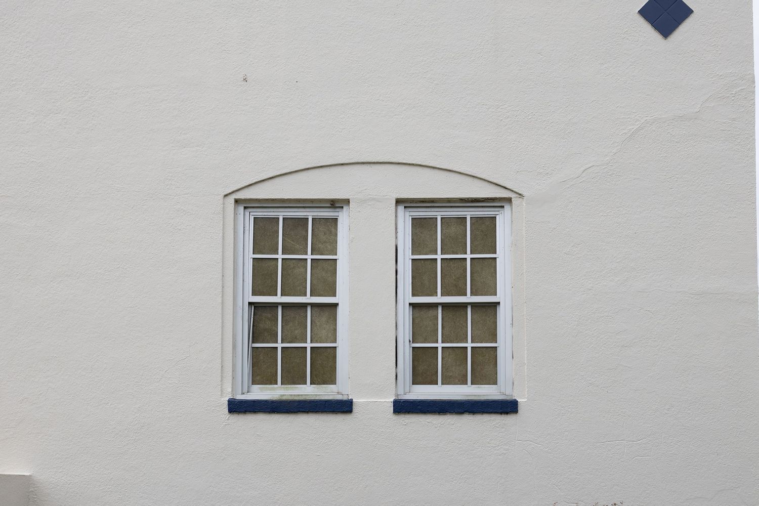White stucco building exterior featuring double arched windows with white frames and blue sills.