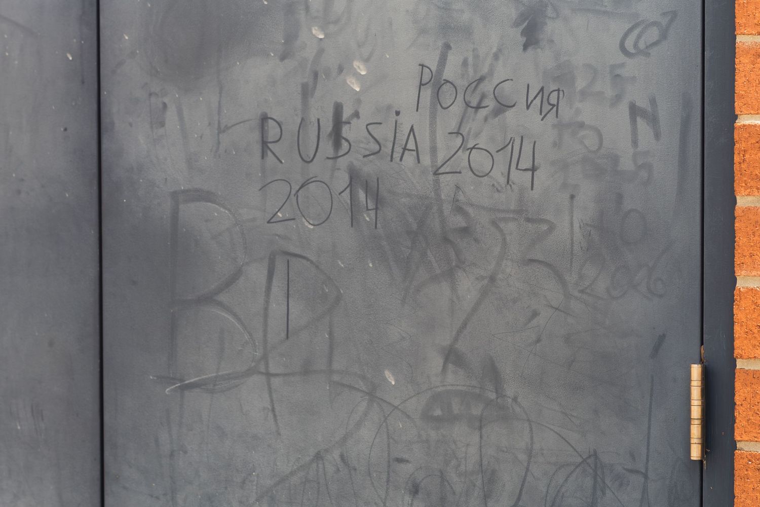 Dark metal door covered in graffiti scratches reading Russia 2014 and Cyrillic text.
