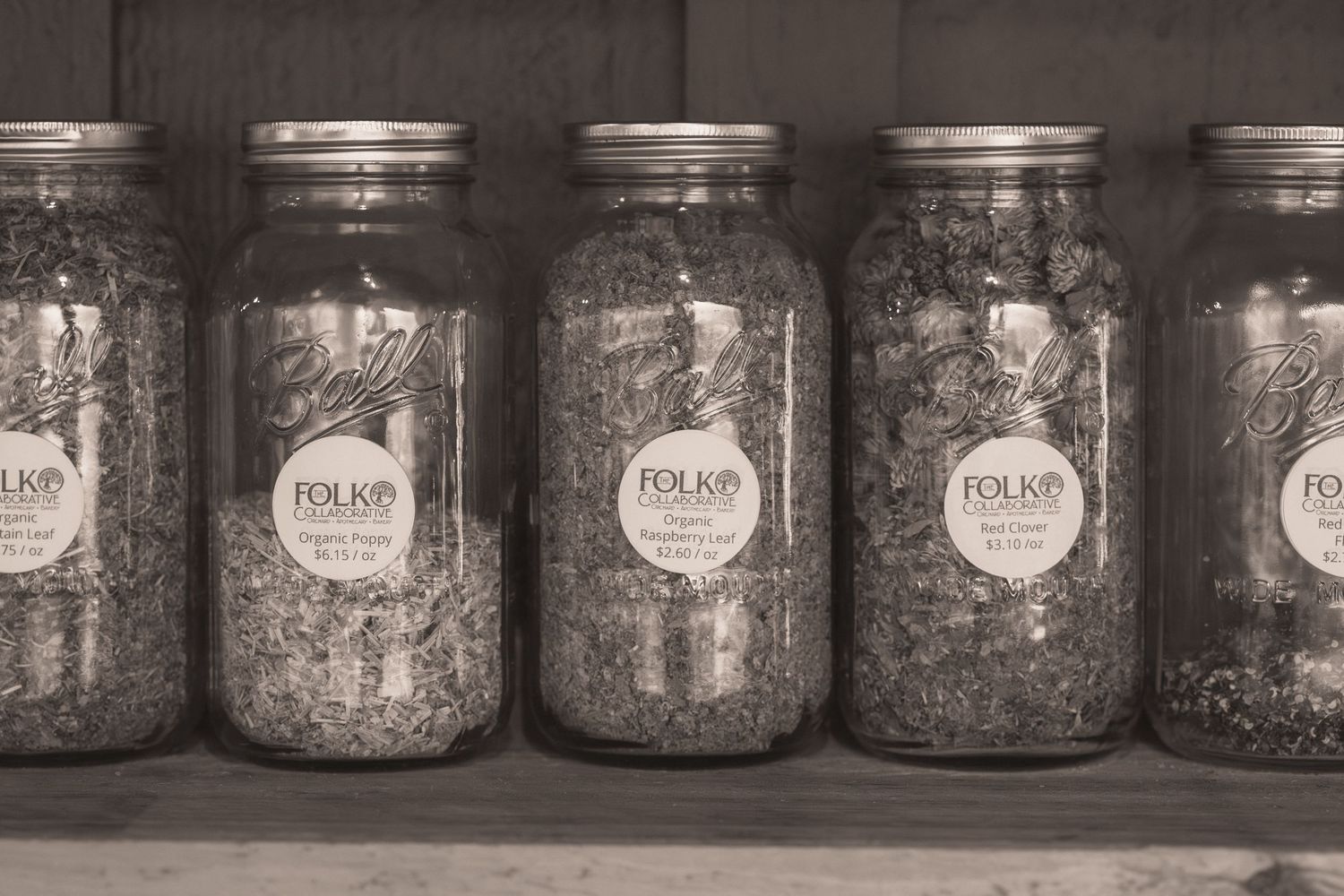 Five Folk brand mason jars filled with dried herbs sit on a wooden shelf in a vintage black and white photo.