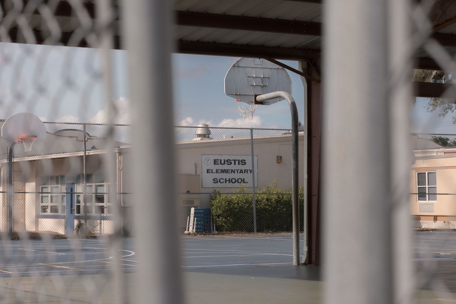 View through chain-link fence of Eustis Elementary School basketball court and building exterior.