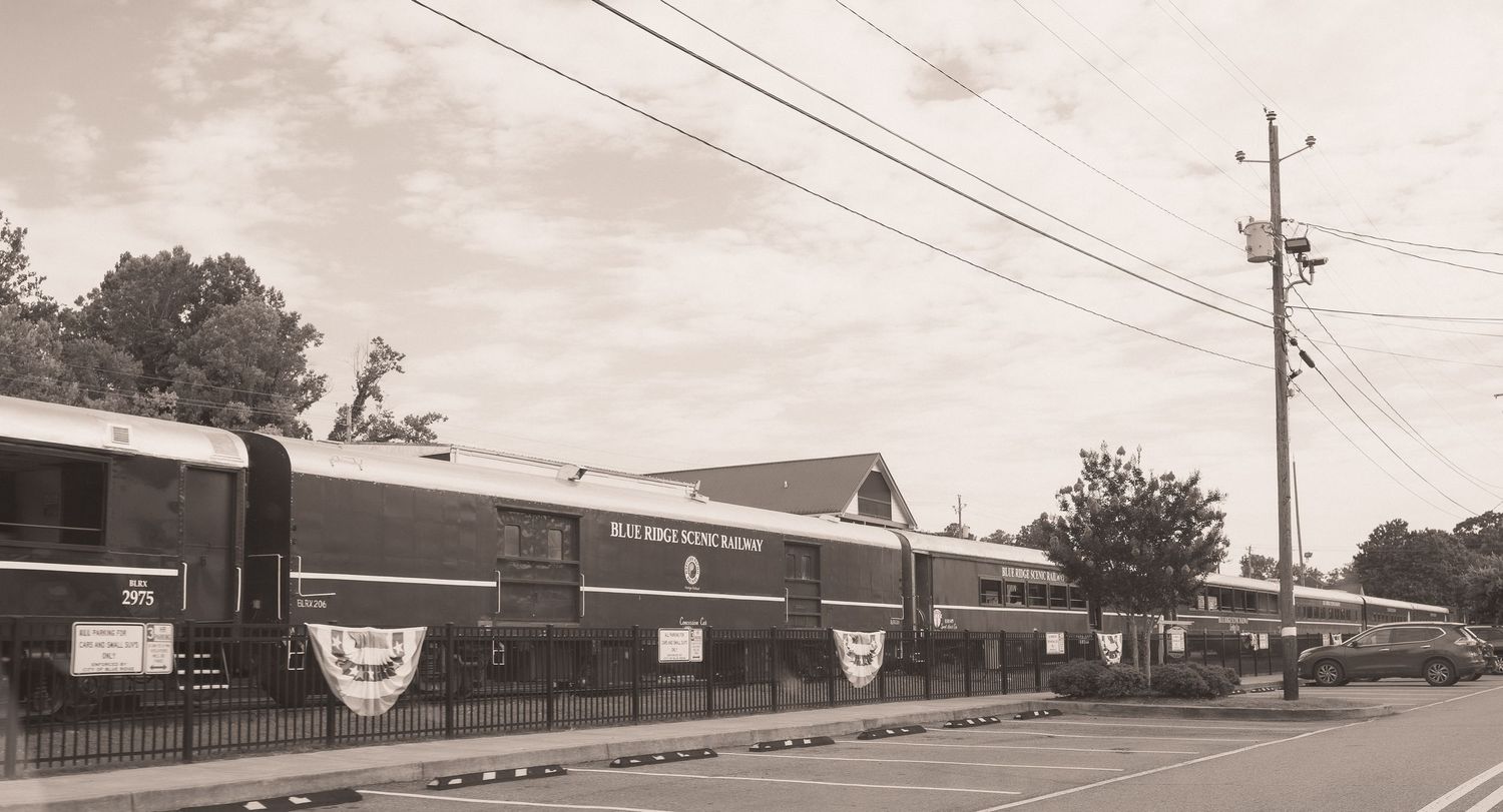 Vintage sepia photo of a classic passenger train parked beside a historic railroad station building.