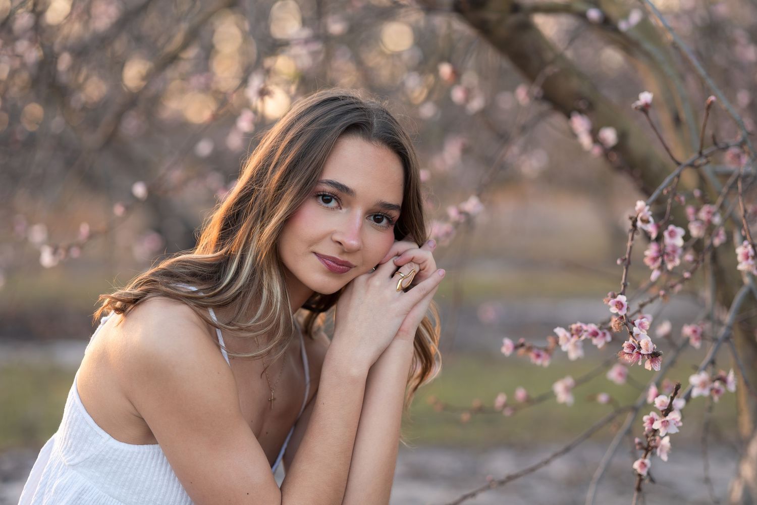 Woman in white dress posing near blooming cherry blossom trees during springtime photoshoot.