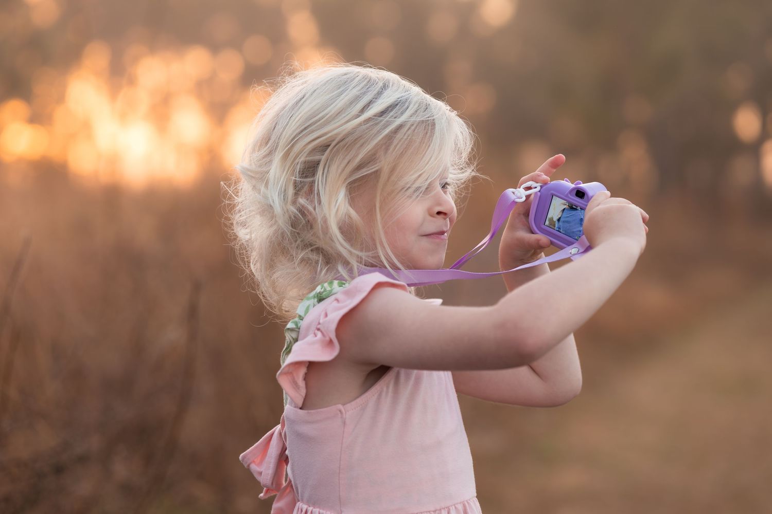 A child in a pink dress plays with bubbles during golden hour in a dreamy outdoor setting.