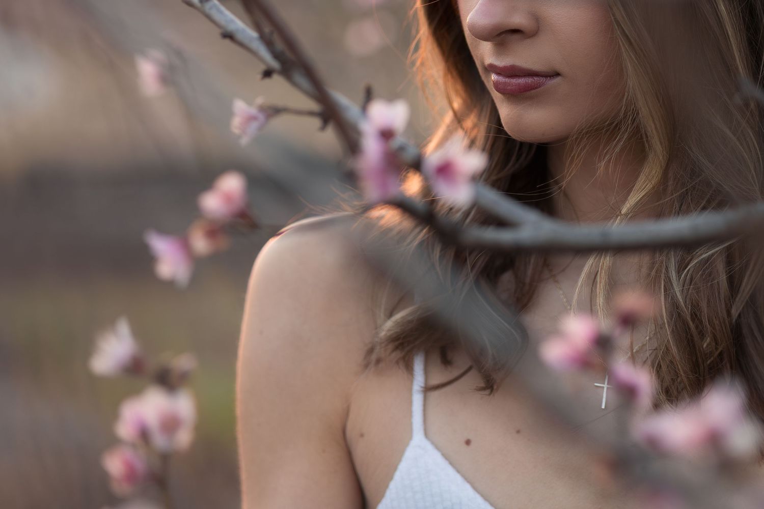 Delicate pink cherry blossoms frame a woman in a white top against a soft blurred background.