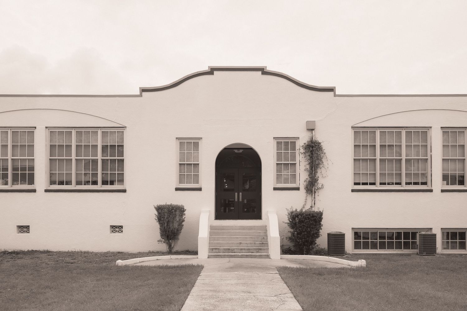 Black and white photo of a classic white Art Deco building with arched entrance, large windows, and manicured lawn.