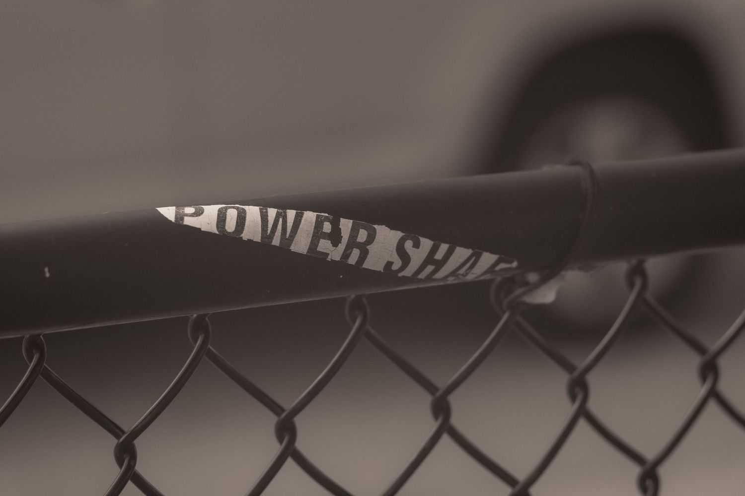 Close-up of a Power Shiv tool resting on a black chain-link fence in sepia tone.