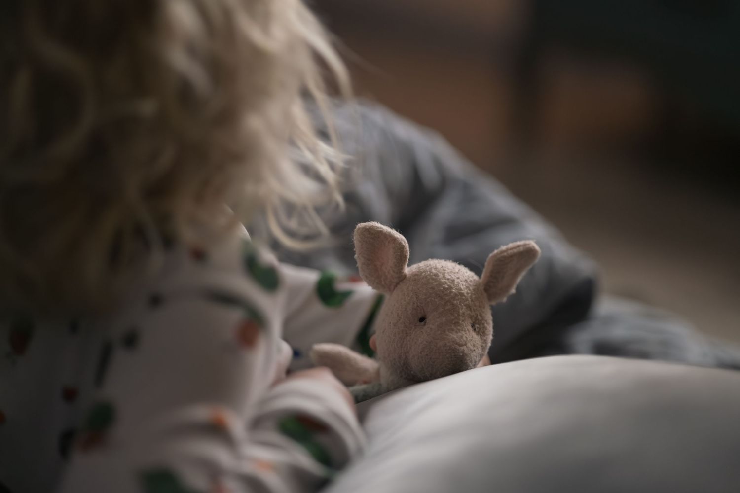 A small plush bunny toy peeks out from between soft bedding in a cozy bedroom setting.