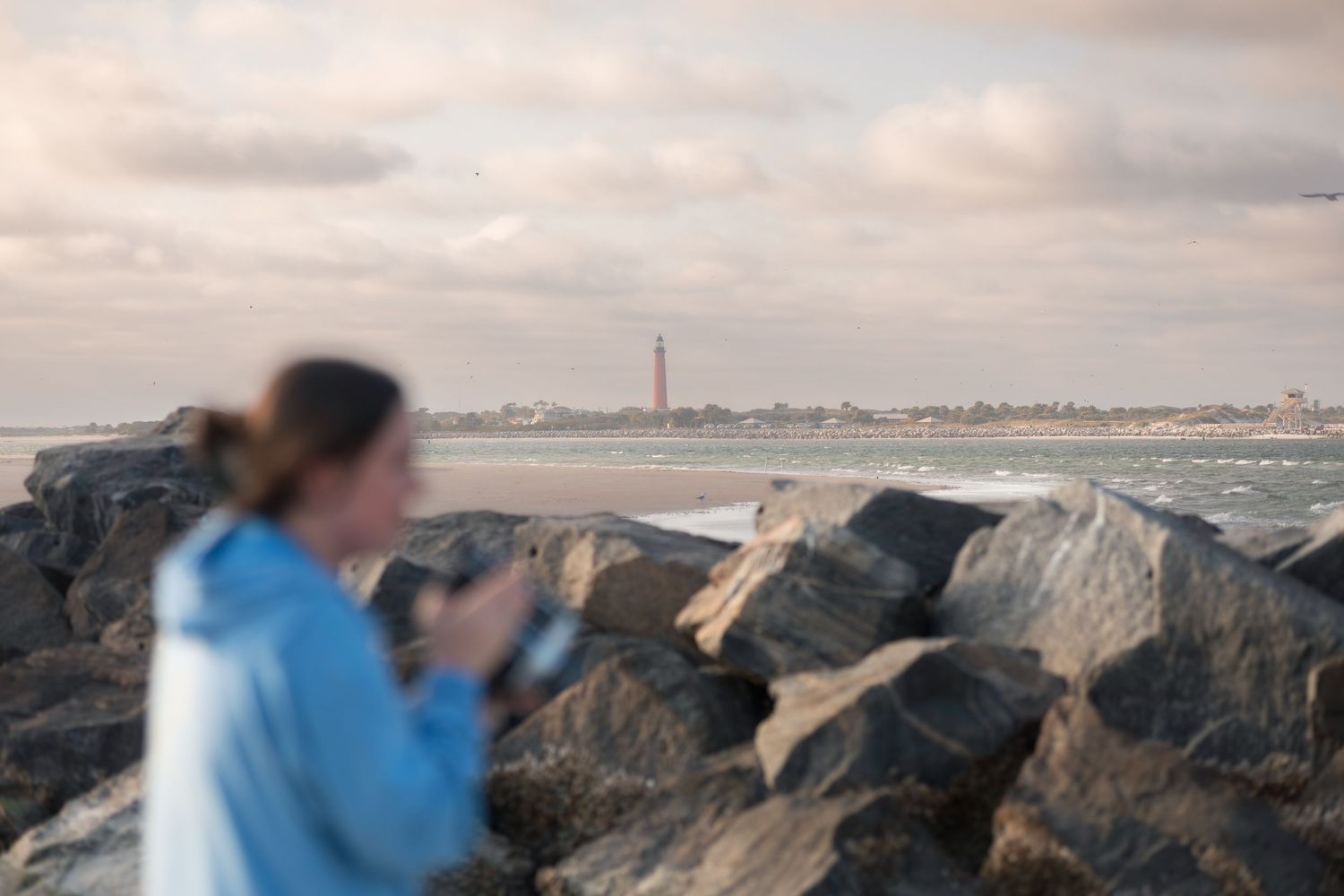 Coastal rocks and waves along a beach shoreline with cloudy skies during sunset.