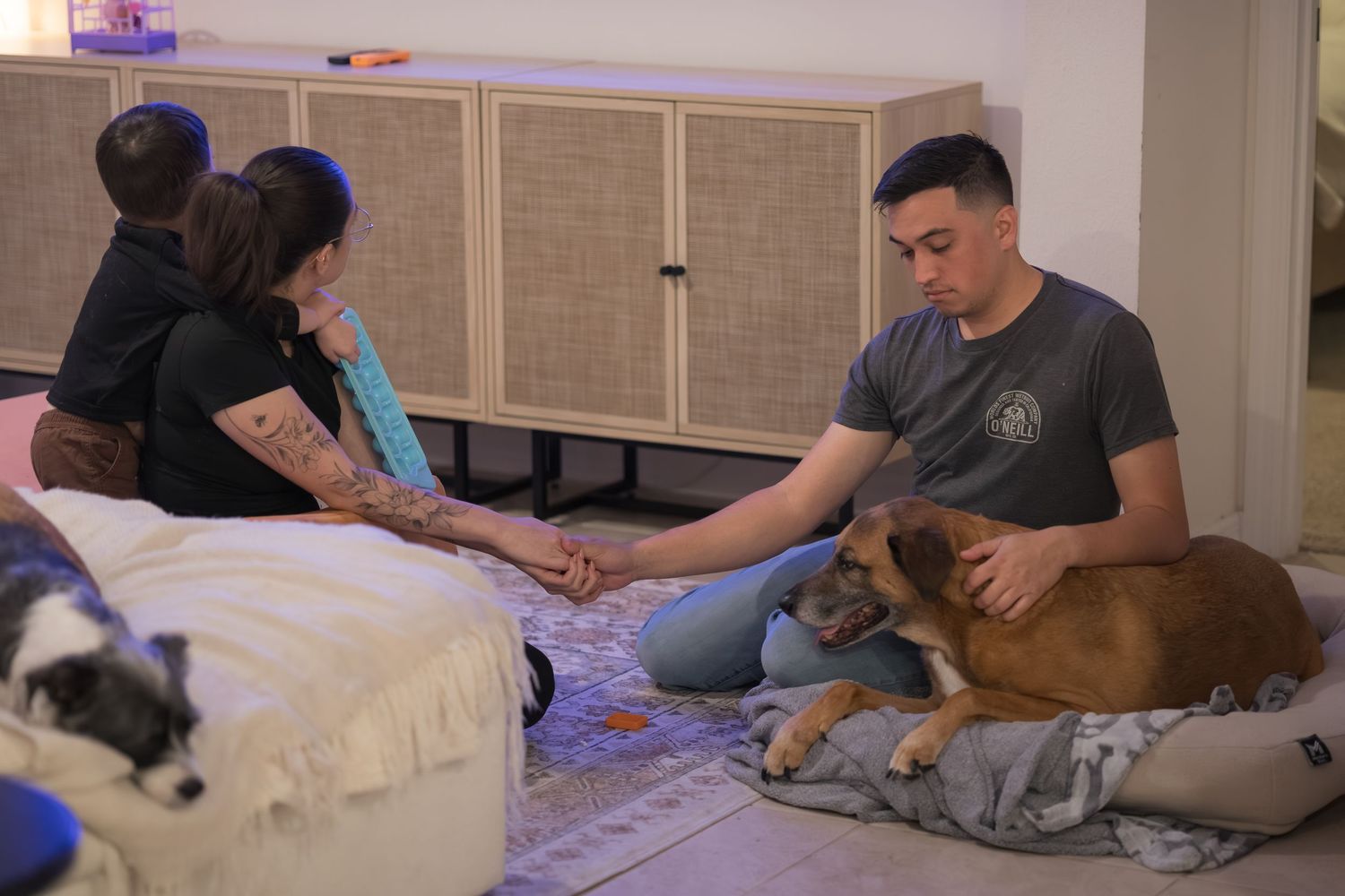 Family and pet dog lounging together on floor cushions during evening activities.