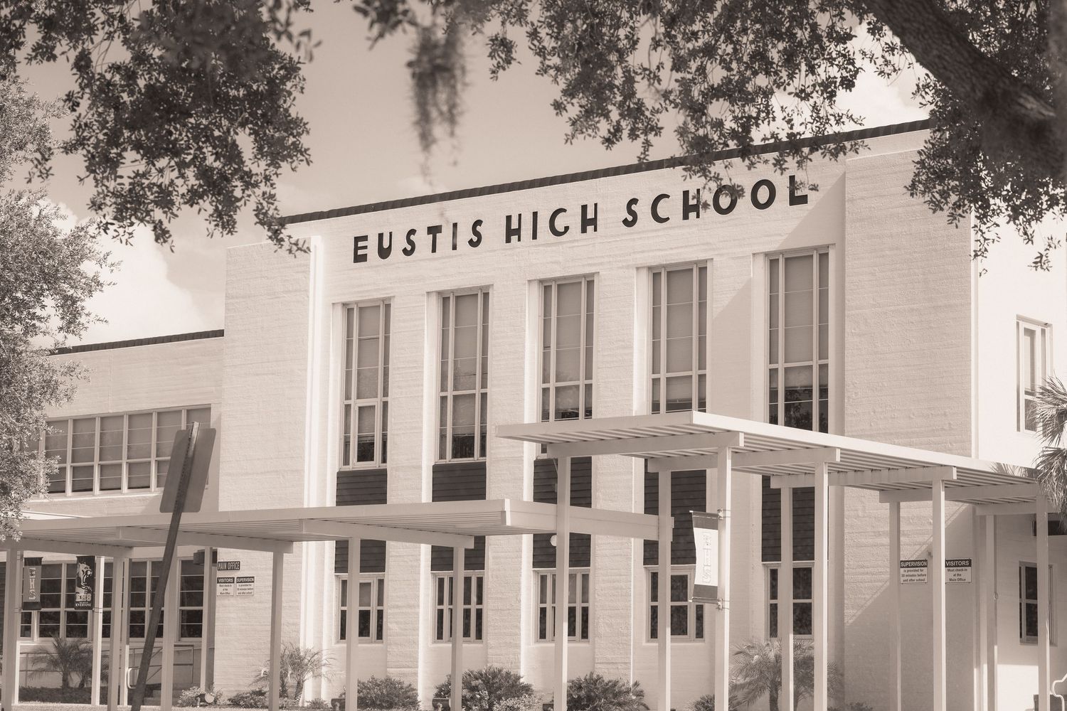Vintage sepia photo of Eustis High School building facade with large sign, windows, and trees in Florida.