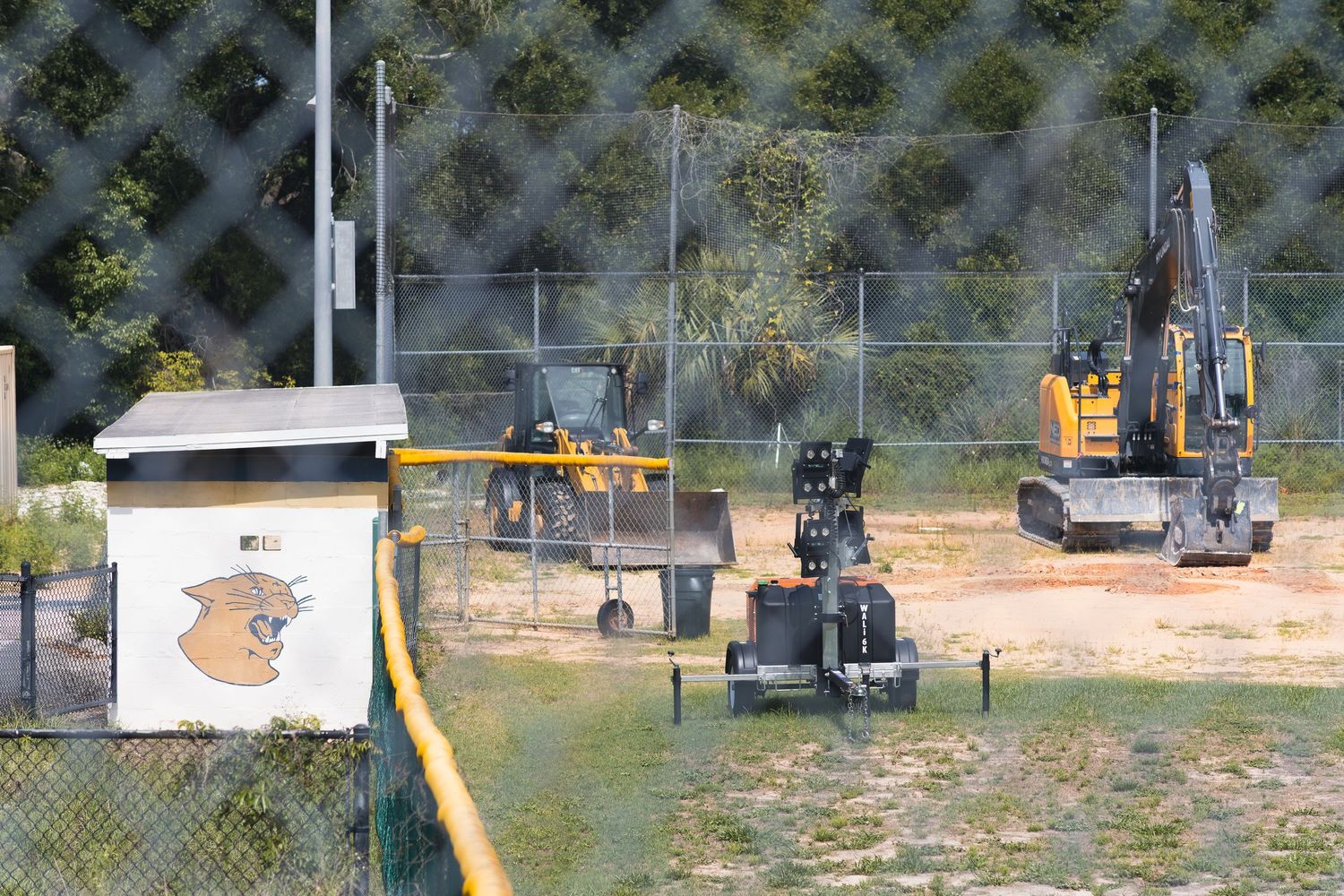 Construction excavator and heavy machinery working on a fenced outdoor site near a building with a logo.