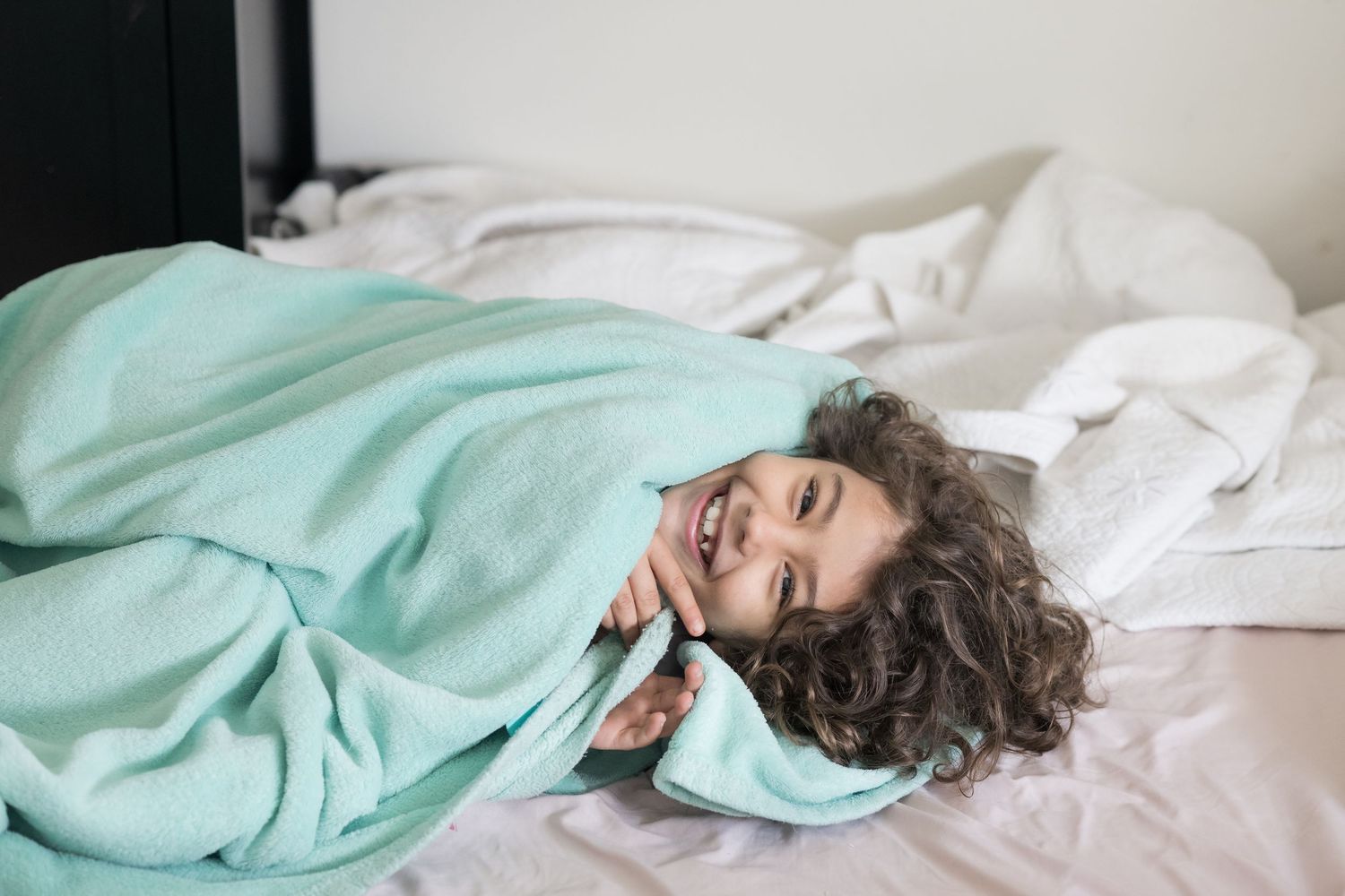 Person lying in bed wrapped in mint green blanket shown in multiple poses against white sheets.