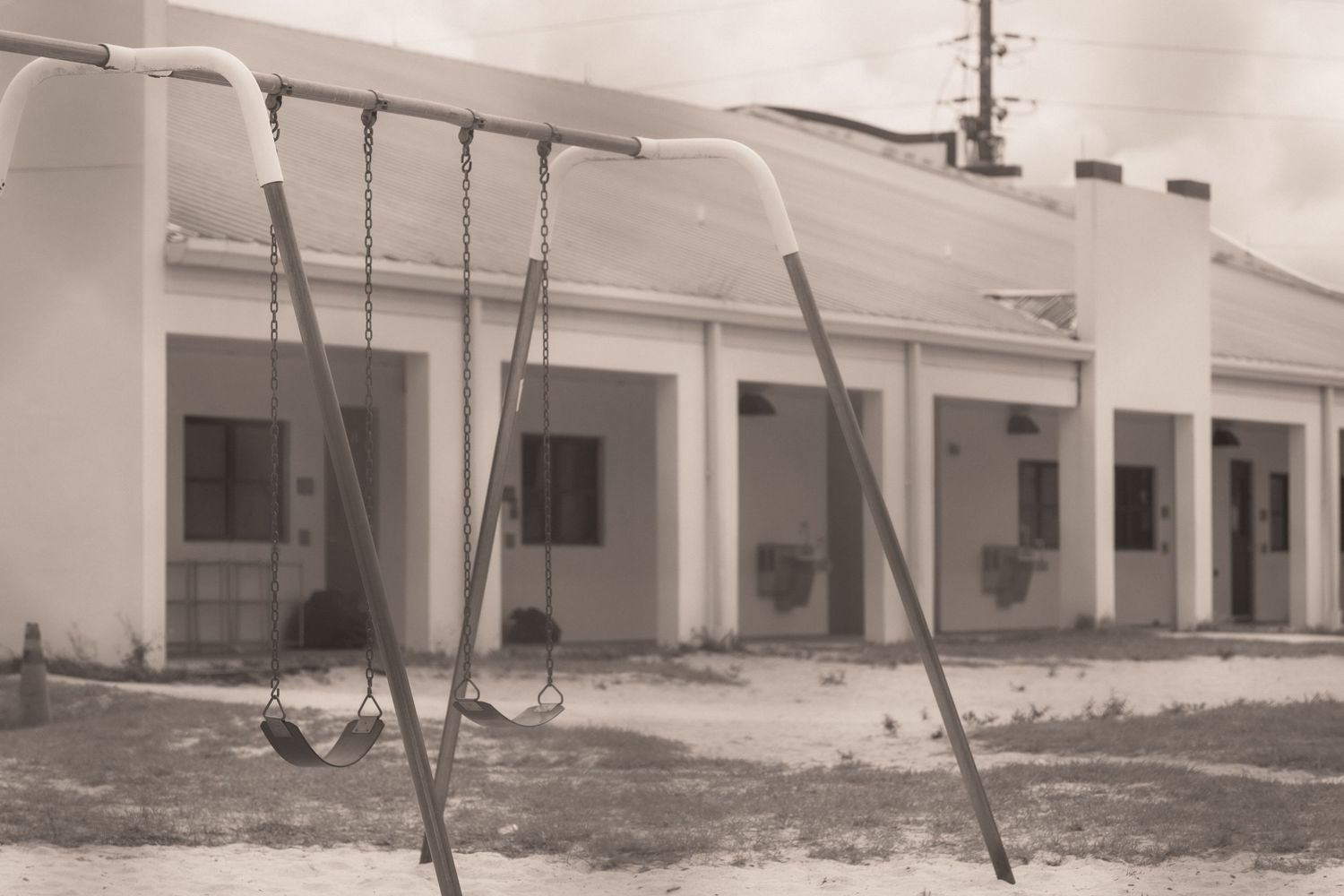 Vintage sepia photo of a motel or school building with metal swing set in sandy playground area.