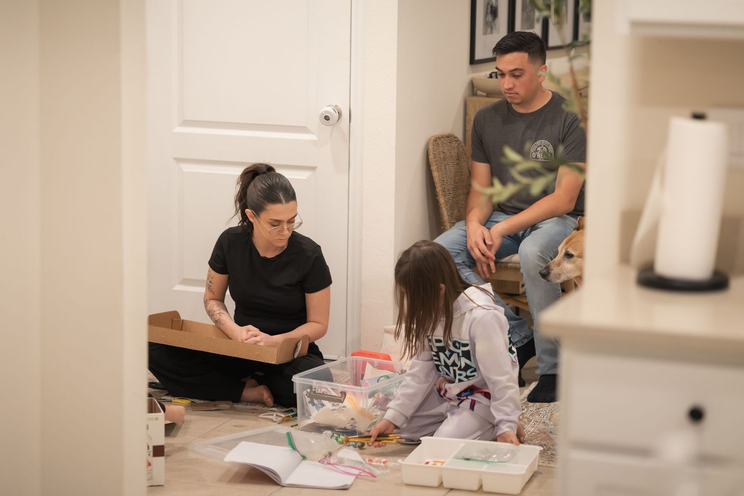 People sit on the floor with books and materials spread out in a home setting.