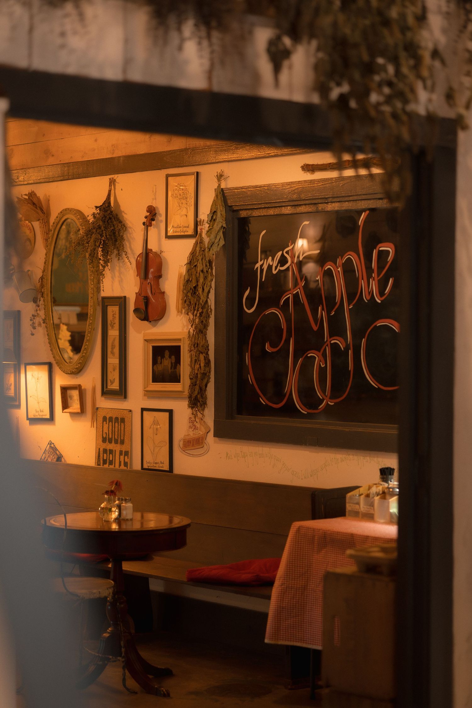 Cozy restaurant interior with violin wall decor, chalkboard sign reading Fresh Apple, framed art, and warm ambient lighting.