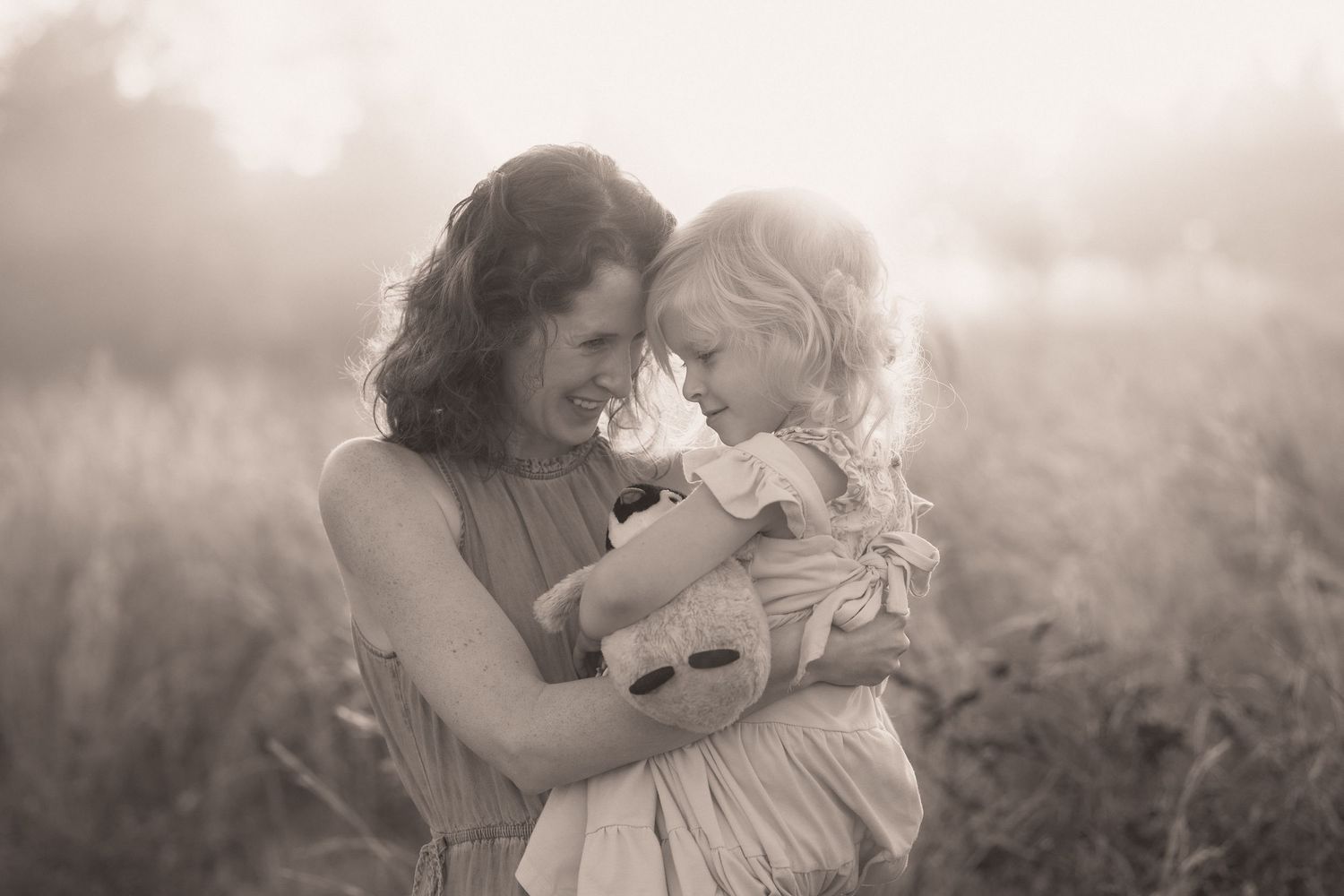 A tender moment between mother and child in a dreamy outdoor setting with soft sunlight filtering through the mist.