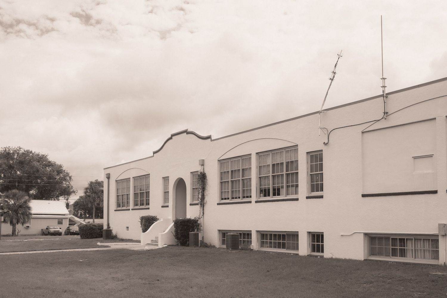Black and white photo of a vintage white Art Deco school building with arched entrance and large windows on a cloudy day.