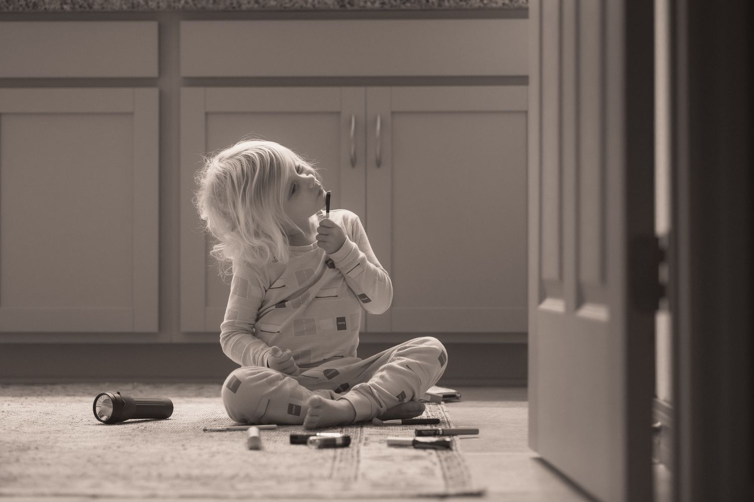 Child sitting cross-legged on floor playing with toy cars in black and white photograph.