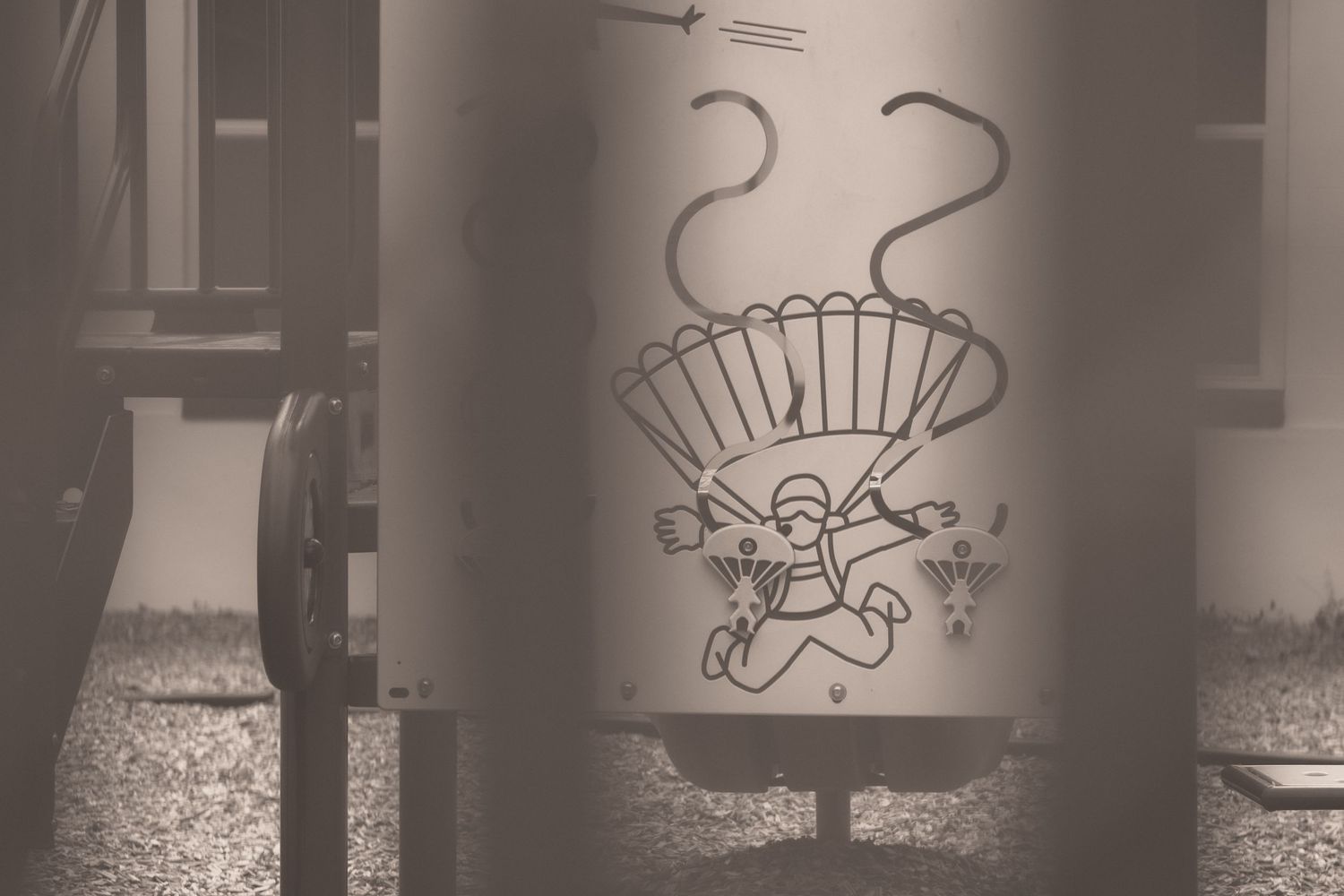 Sepia-toned industrial cylinder with graffiti art depicting a parachuting figure, outdoors.