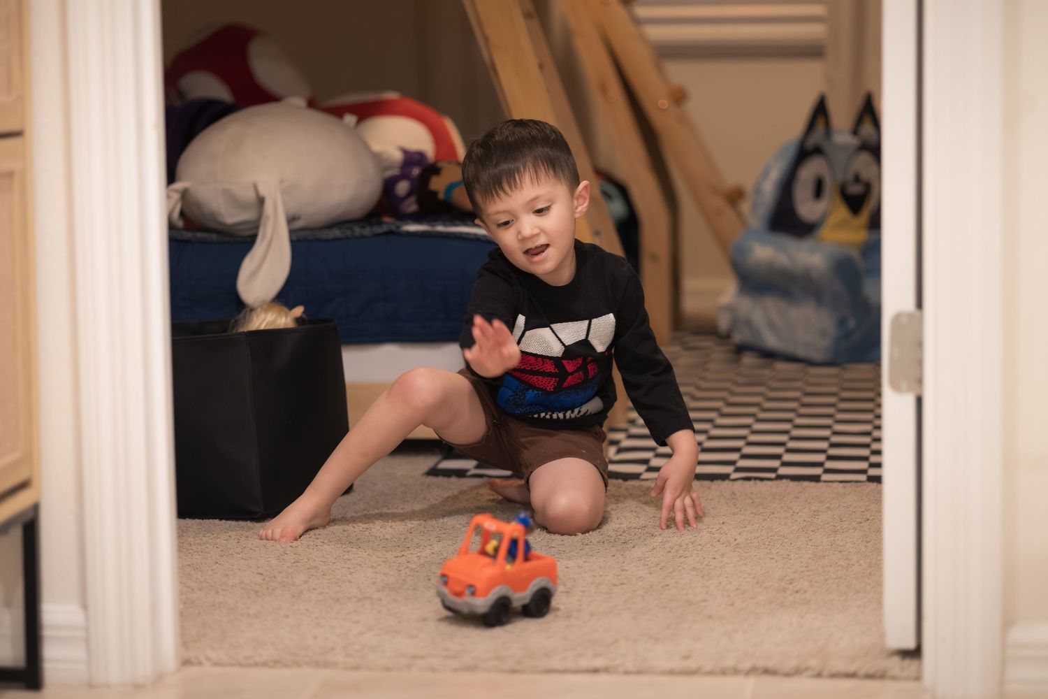 A small child plays with a toy truck on carpeted floor near a doorway.
