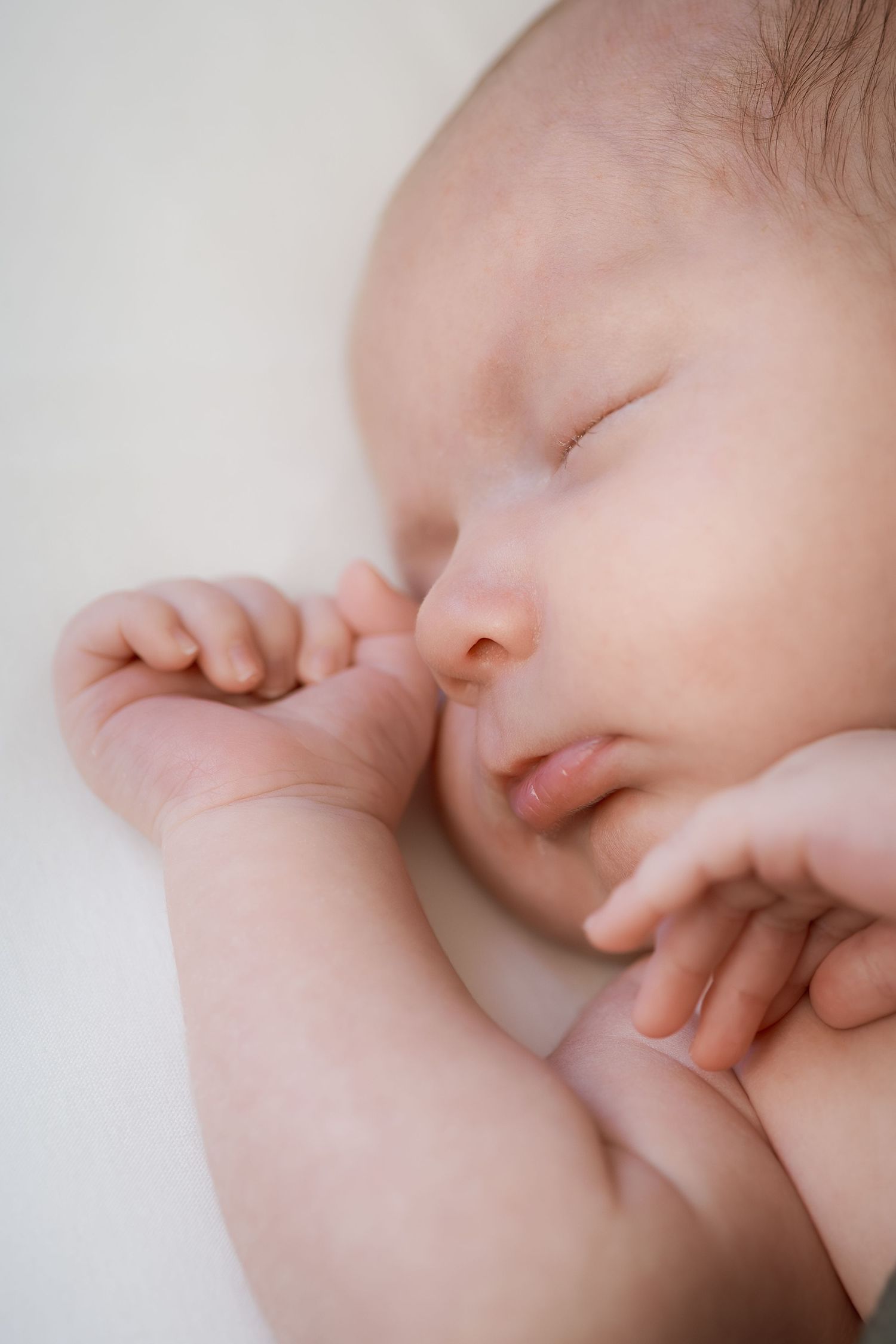 A sleeping baby's face in close-up view with tiny fingers near their mouth in a peaceful resting position.