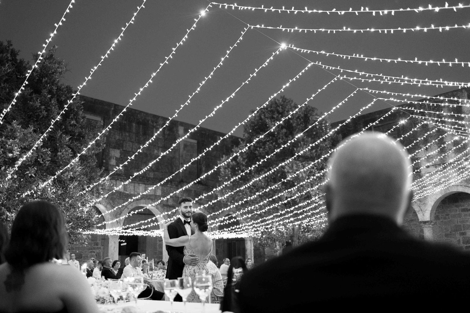 Decorative string lights create a glowing canopy overhead at an outdoor evening event space.