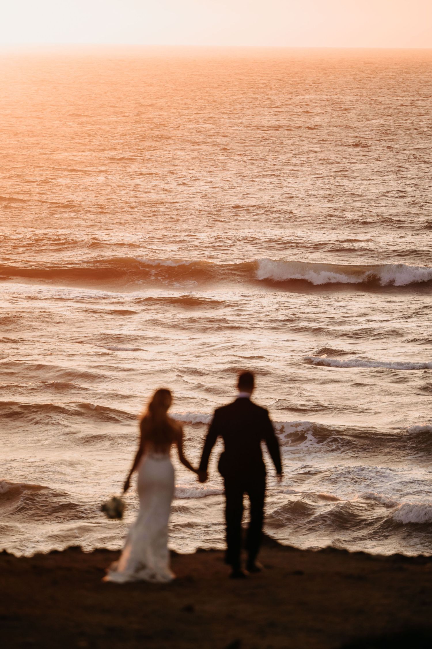 Silhouettes of a couple walking along a beach at sunset with warm orange tones.