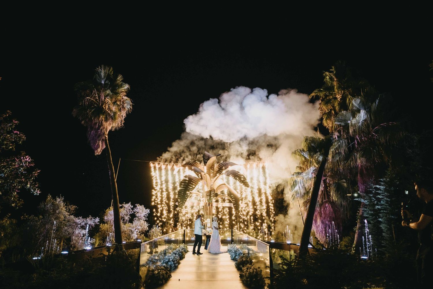 Nighttime wedding venue illuminated with string lights and palm trees creating magical atmosphere.