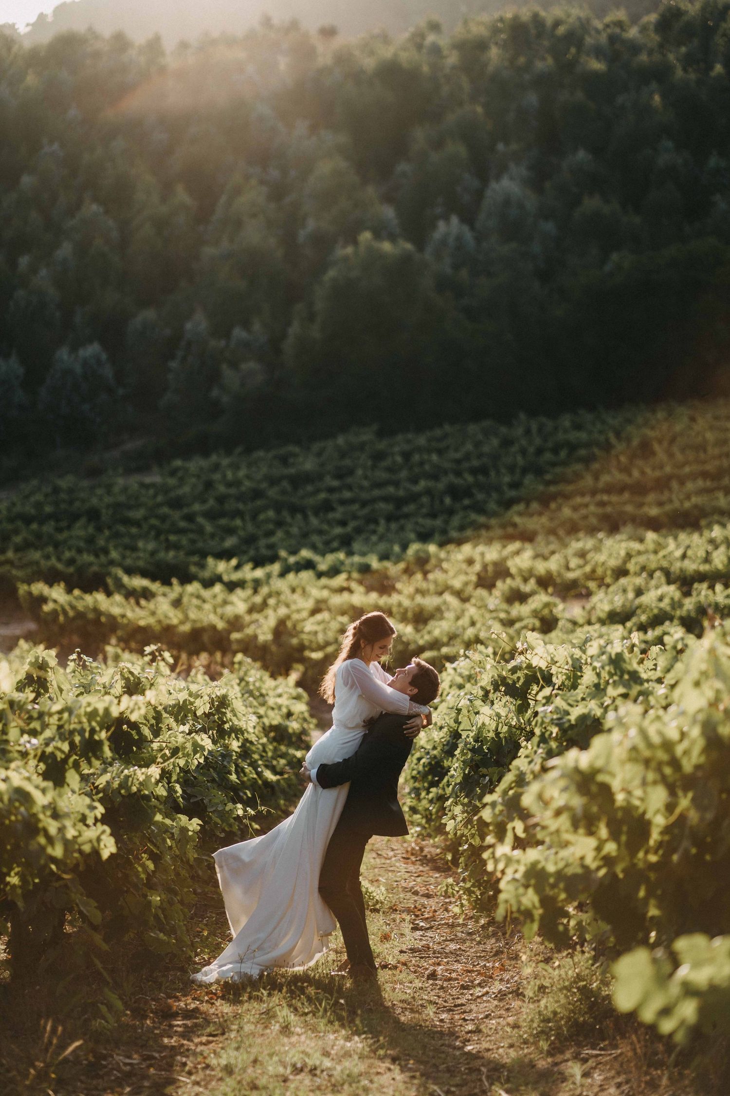 Couple dancing in a sunlit vineyard with rolling hills in the background.