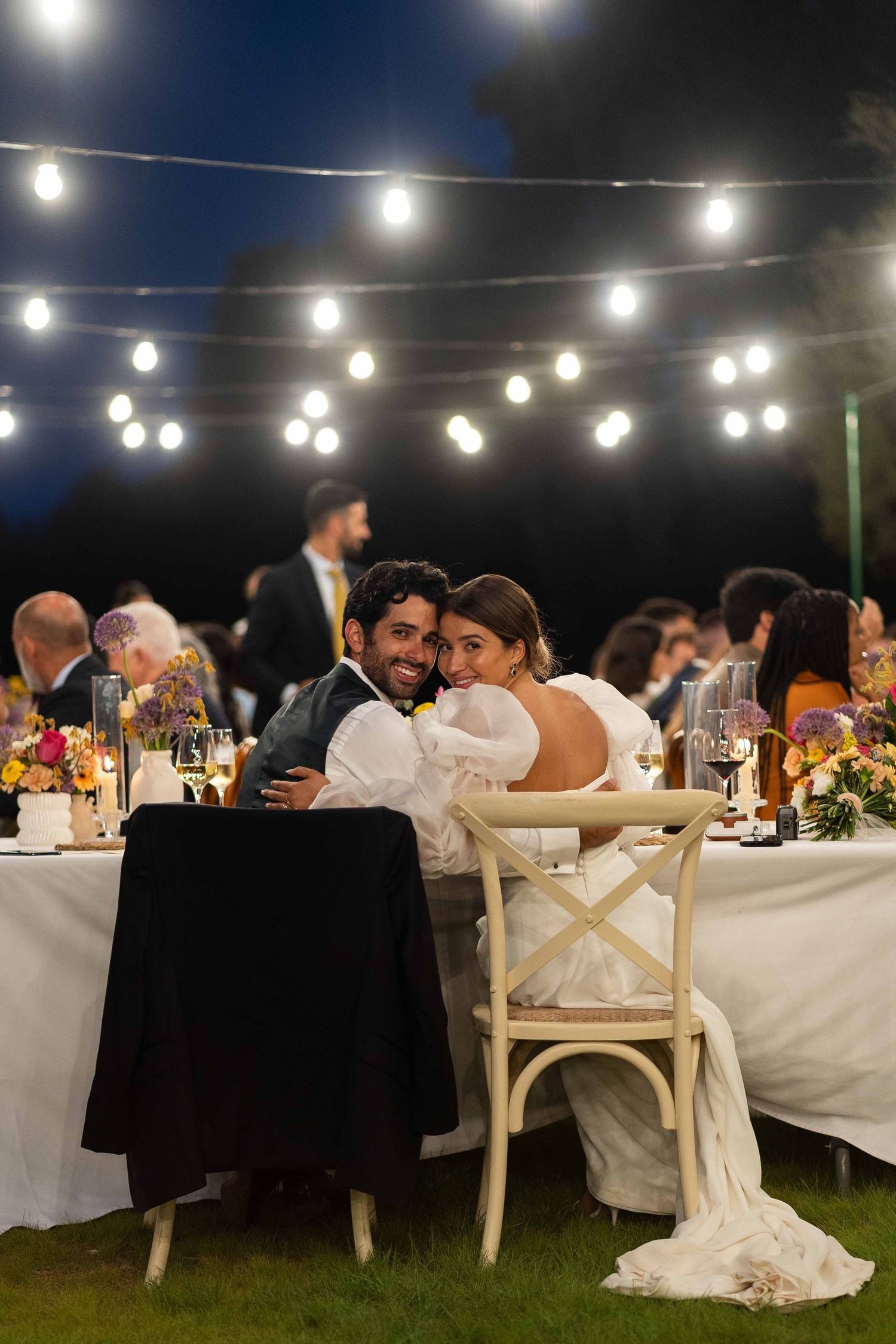 Evening outdoor wedding reception under string lights with elegant table settings.
